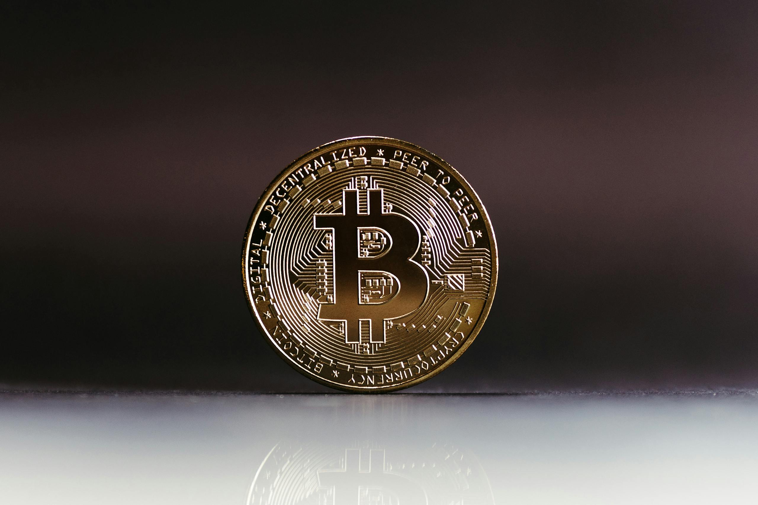 A close-up of a shiny Bitcoin coin on a reflective surface, highlighting cryptocurrency finance.